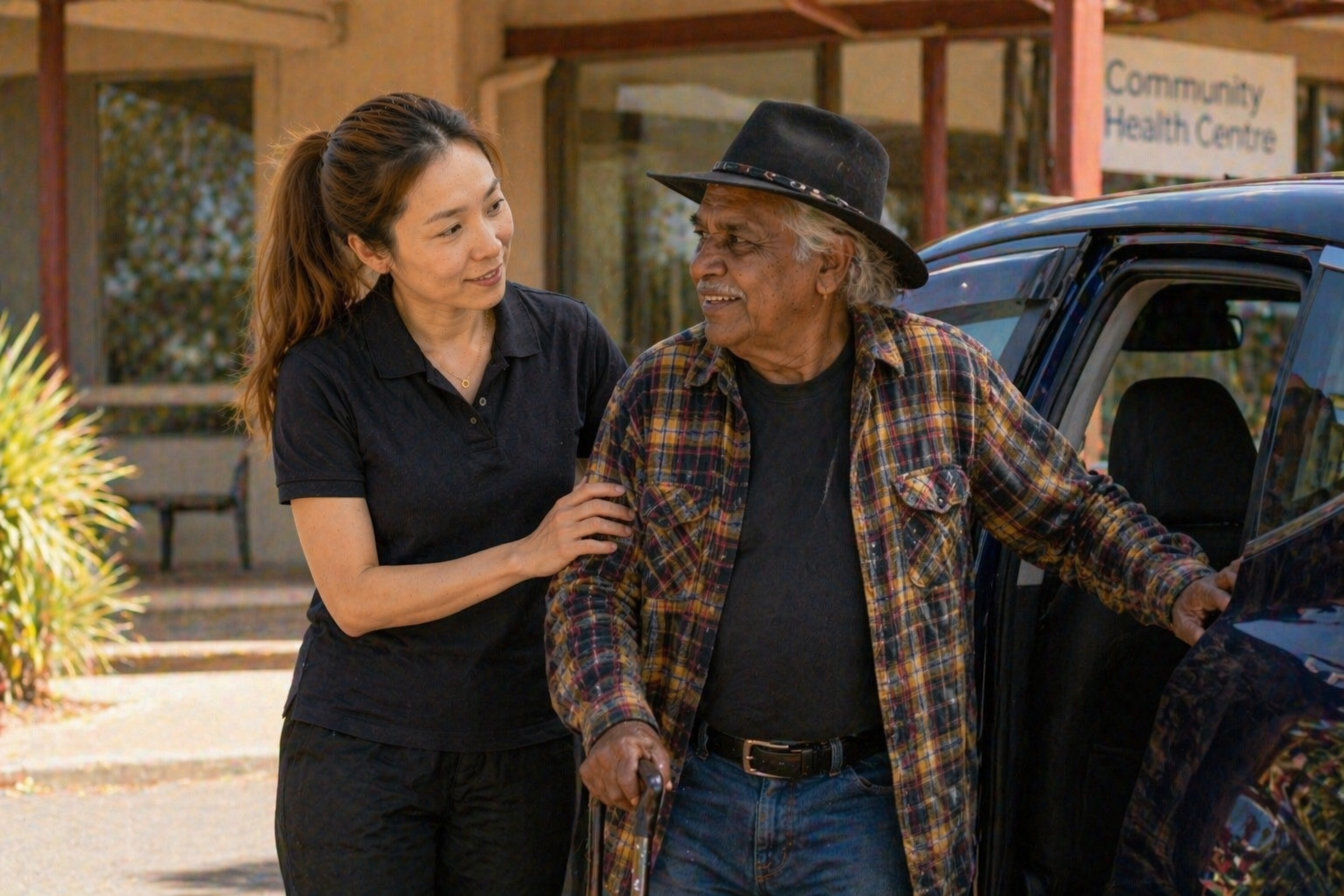 Support worker assisting Indigenous elderly man into vehicle outside Community Health Centre — transport assistance Melbourne